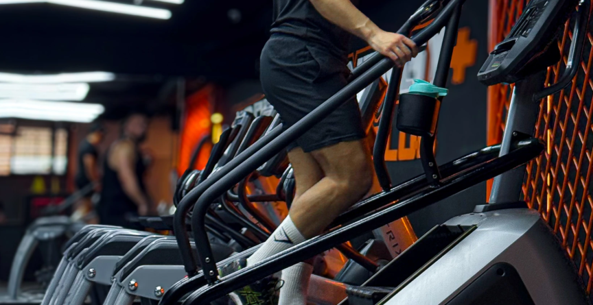 Bahae Sthetic en t-shirt noir et short sur une machine à escaliers en salle de sport